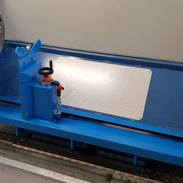 Contro una parete liscia si trova una macchina industriale blu con base in metallo e vari componenti, tra cui una maniglia e delle manopole. Per la lavorazione di parti metalliche sembrano essere utilizzate le attrezzature personalizzate, dotate di mandrino e pannelli di protezione. I dintorni sono puliti e ben tenuti.