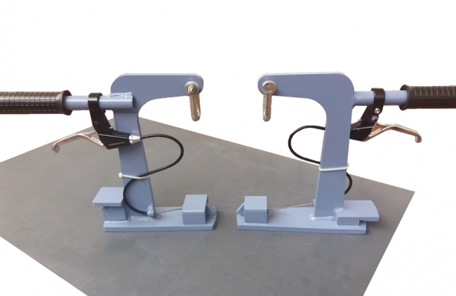Un paio di morsetti da palestra blu con maniglie e leve nere sono visualizzati su una superficie piana. Ogni attrezzatura personalizzata presenta un bullone nella parte superiore, un meccanismo di bloccaggio curvo e un filo a spirale fissato al manico. Sono posizionati simmetricamente, uno di fronte all'altro.